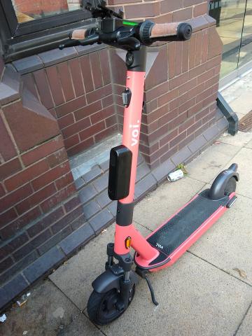 Voi electric hire scooter parked against a wall