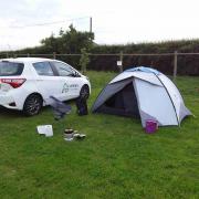 A white Toyota Yaris parked in a camping field next to a white 3-person tent