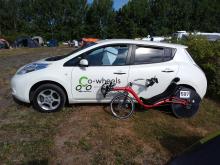 Optima Baron recumbent bicycle leaning against a white Nissan Leaf with a Co-Wheels Birmingham logo